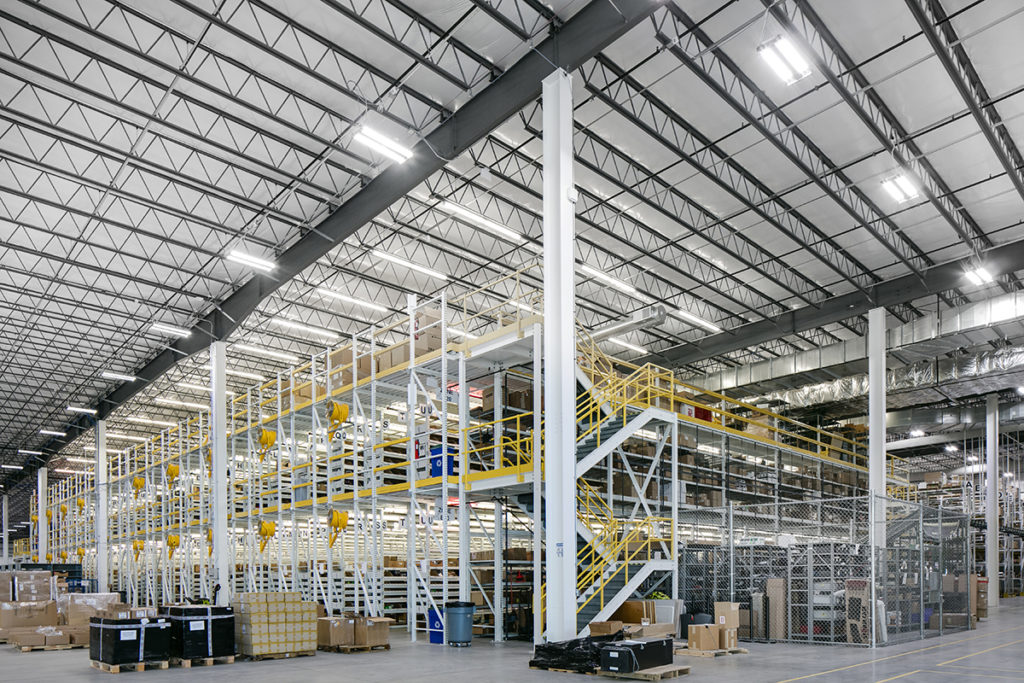 Modern warehouse interior with multi-level mezzanine, yellow safety railings, and high-bay racking for distribution operations.